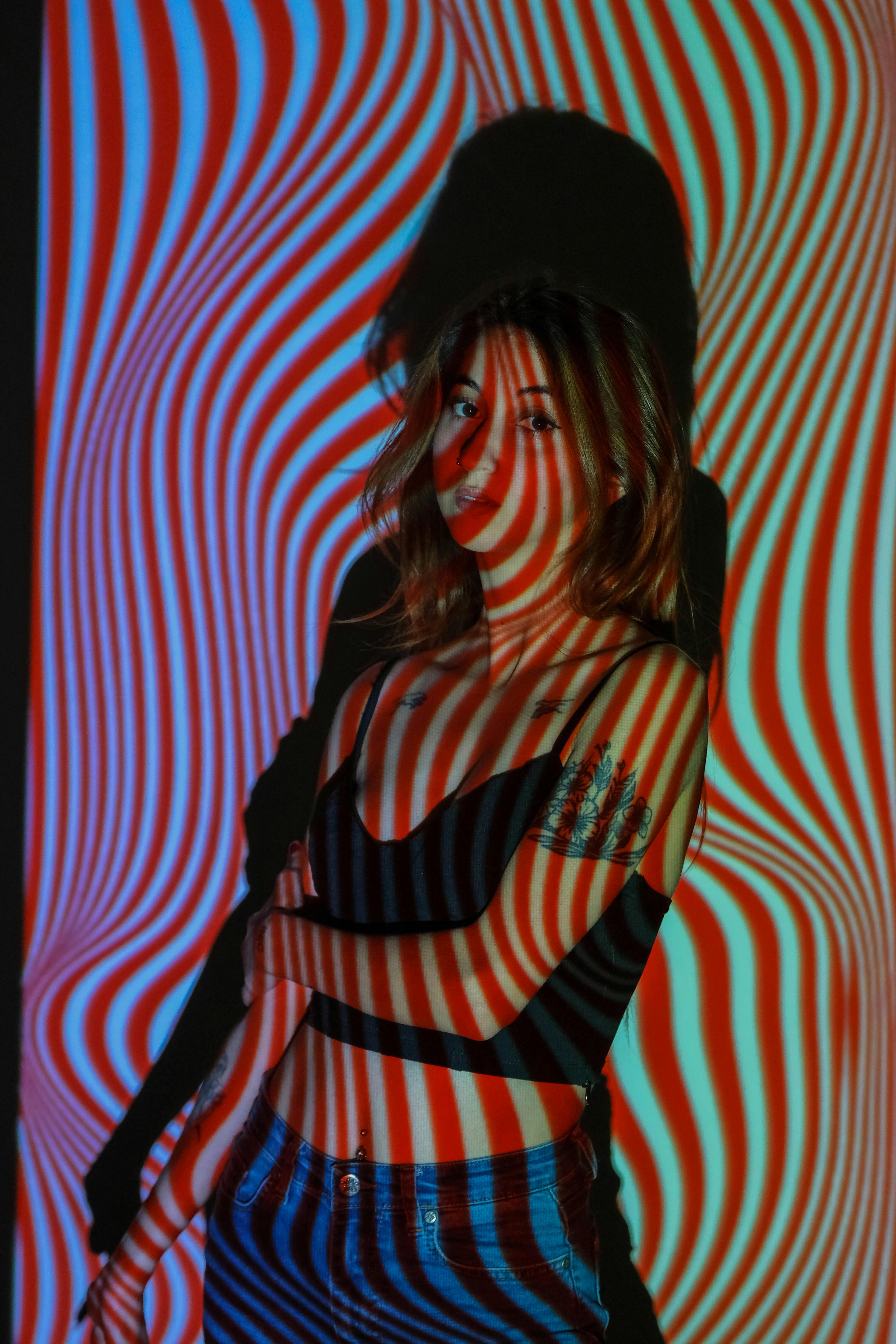 Woman standing indoors with vibrant psychedelic pattern projected on her.