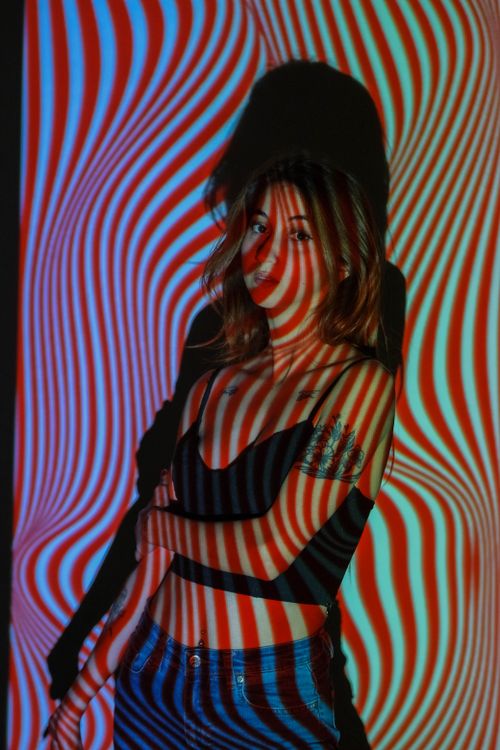 Free Woman standing indoors with vibrant psychedelic pattern projected on her. Stock Photo