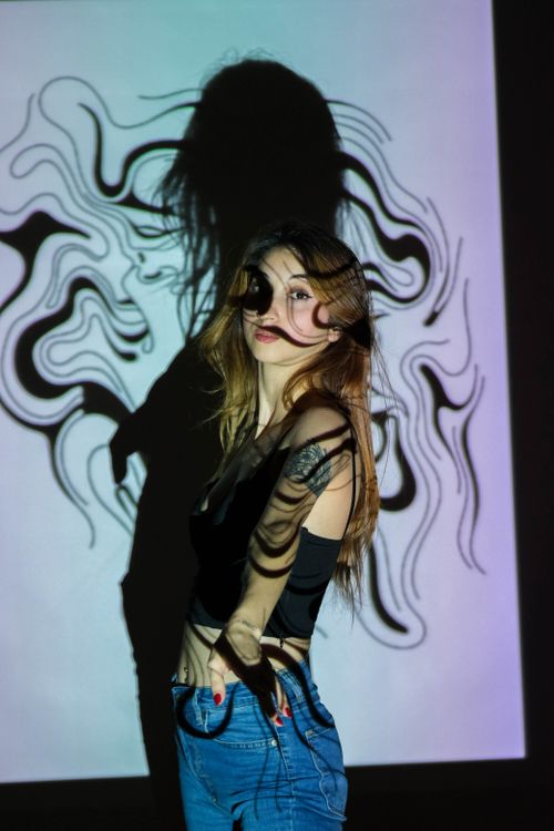 Free A woman poses against a projected abstract design, casting shadows, in an Ankara studio. Stock Photo