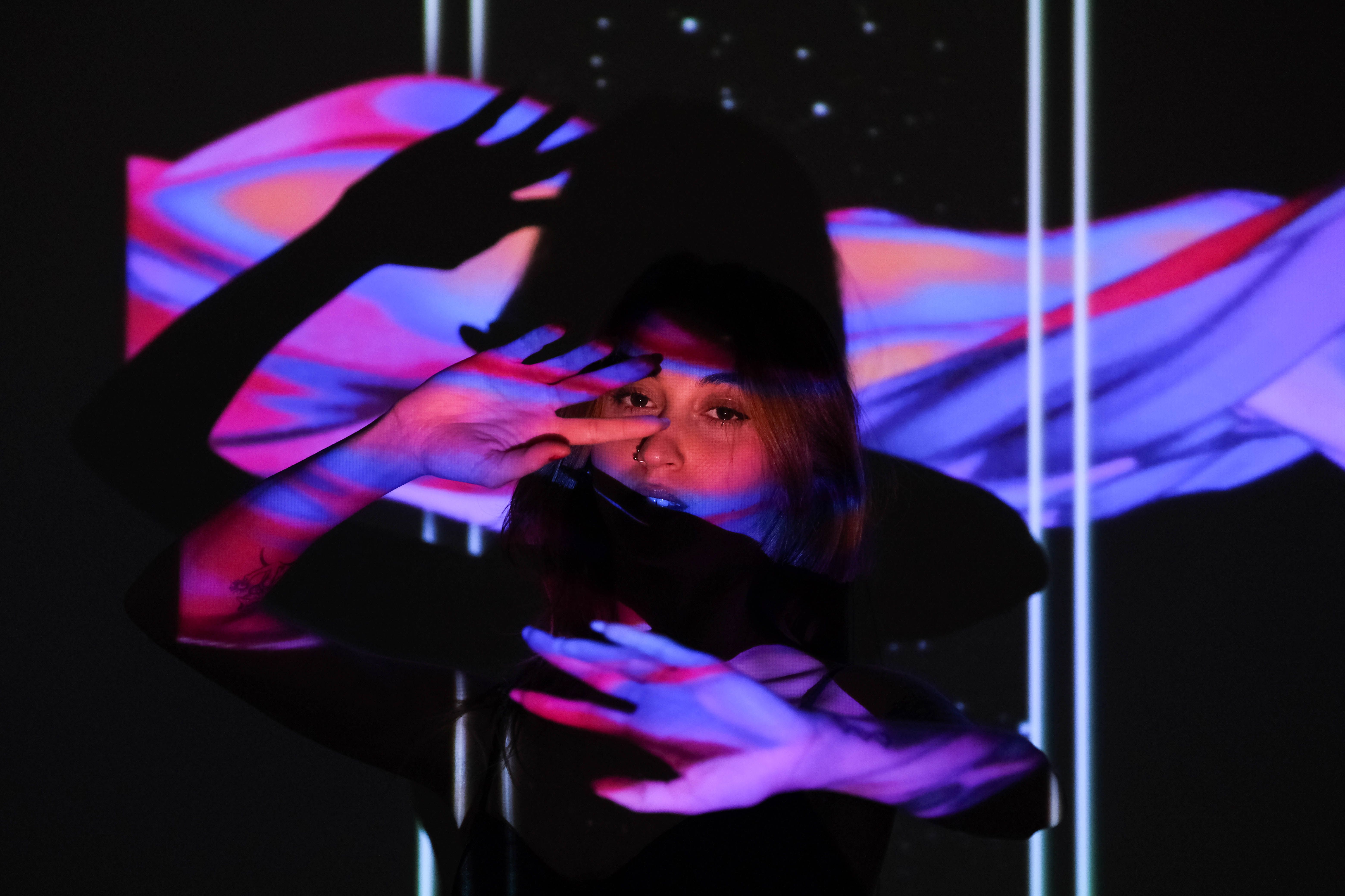 A striking artistic portrait featuring vibrant abstract projections casting colorful patterns on a woman indoors.