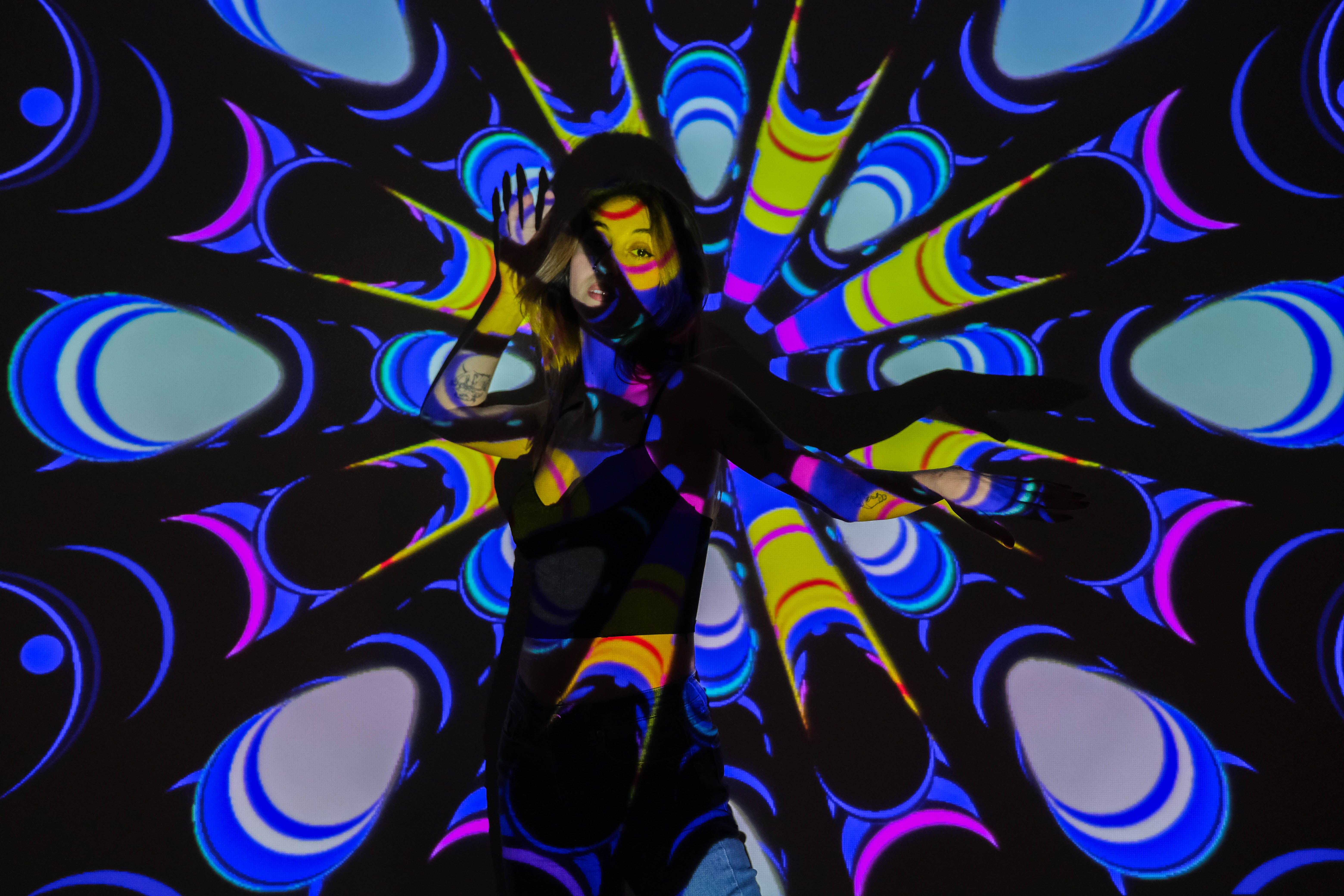 A vibrant artistic projection on a model posing indoors, creating colorful patterns.