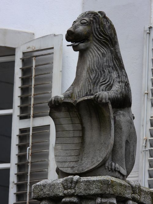 Free A detailed stone sculpture of a lion holding a shield against a building background. Stock Photo