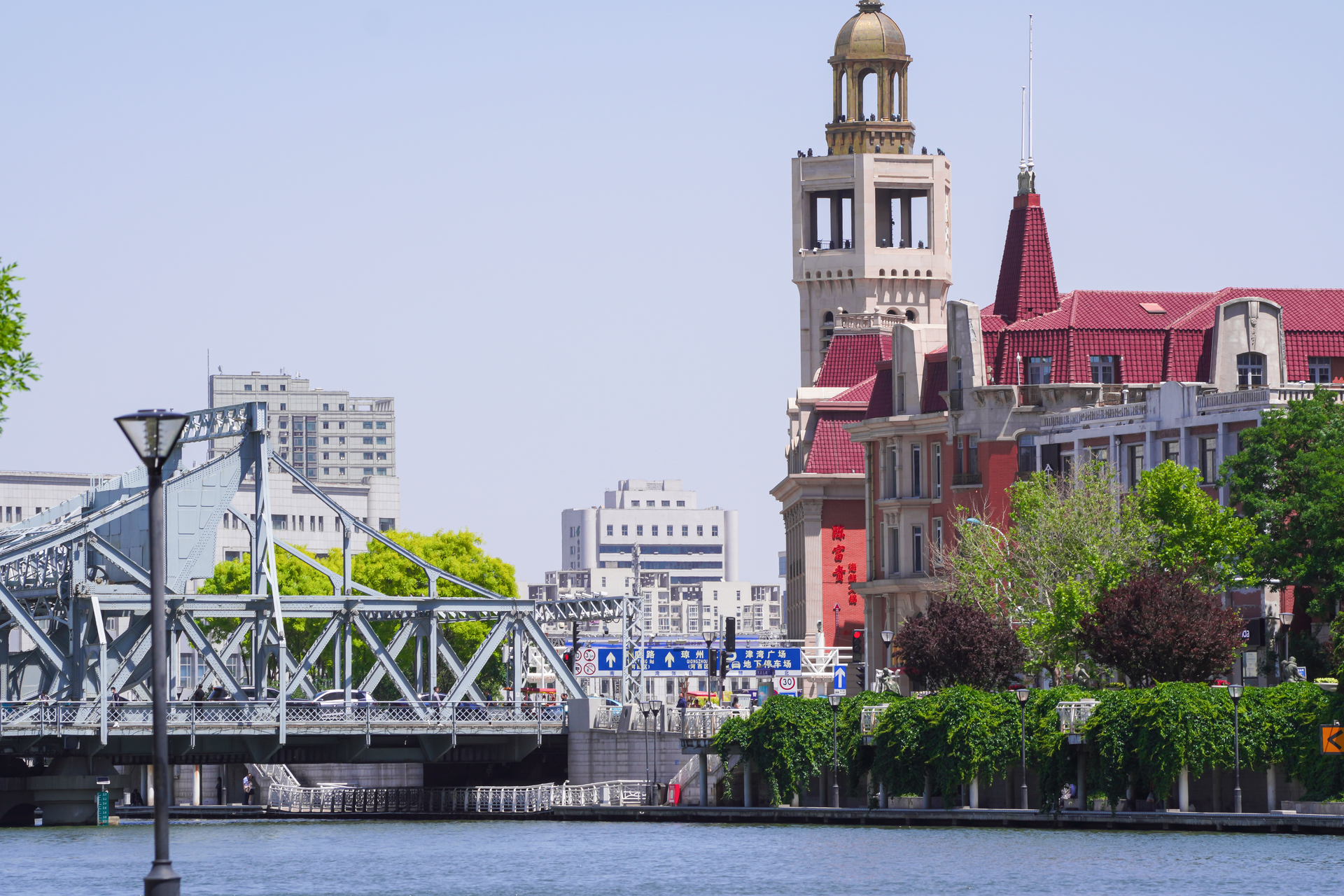 A vibrant cityscape of Tianjin featuring a historic bell tower, steel bridge, and lush greenery.
