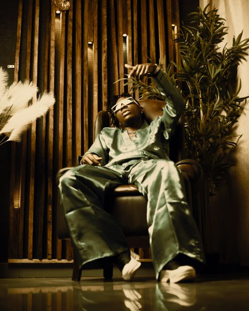 Free Fashionable man wearing green satin suit and sunglasses, lounging in a leather armchair indoors. Stock Photo