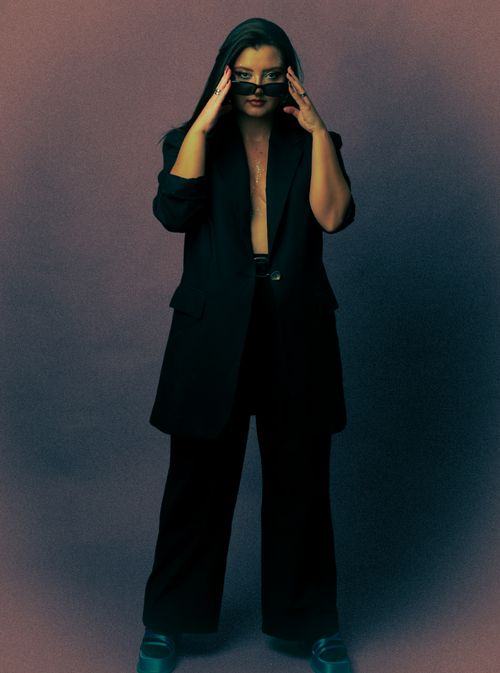 Free Fashion portrait of a woman with black hair posing in a studio wearing a suit and sunglasses. Stock Photo