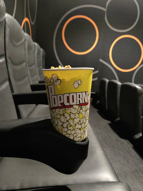 yellow paper cup with popcorn on a cinema seat