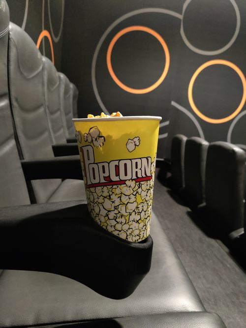 Free A bucket of popcorn sits alone on a cinema seat in a modern theater setting. Stock Photo