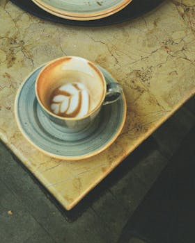 Artistic latte in a cup with leaf design on a marble table. Cozy and inviting.