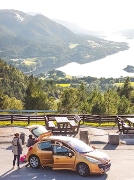 Breathtaking view of Norway's mountains with travelers and a car at a roadside stop.