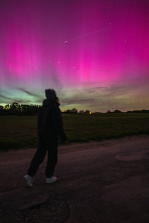 A person walking down a road with the aurora borealis in the sky