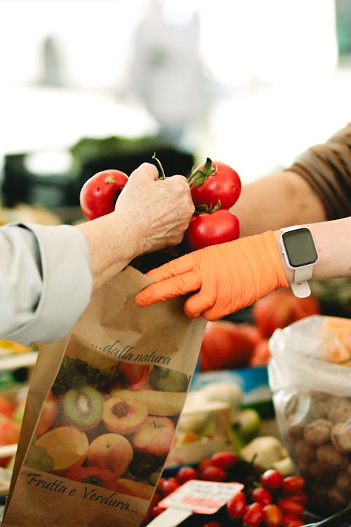 A woman is holding a bag of tomatoes and gloves