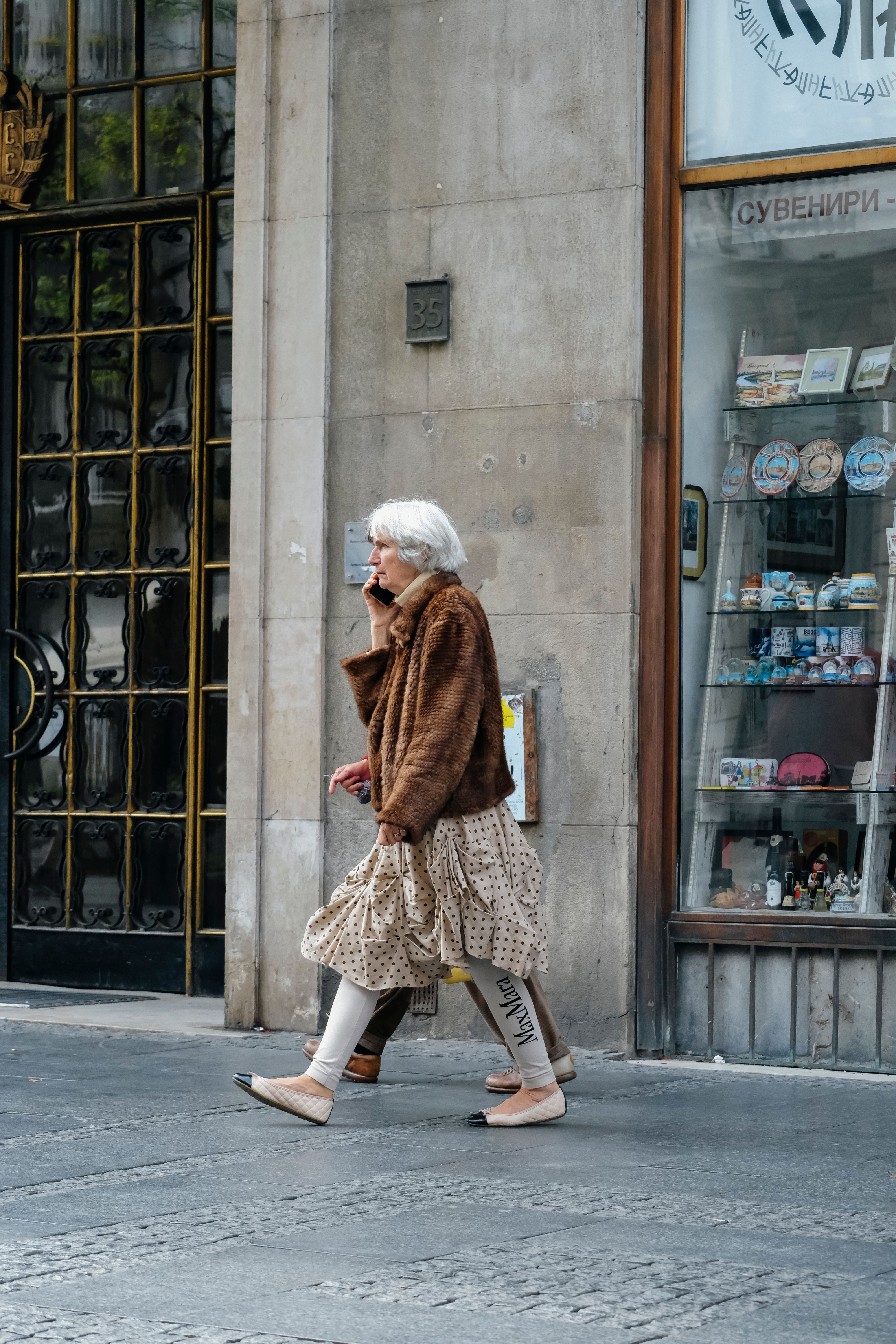 Senior woman with gray hair in urban setting, walking past shopfront.
