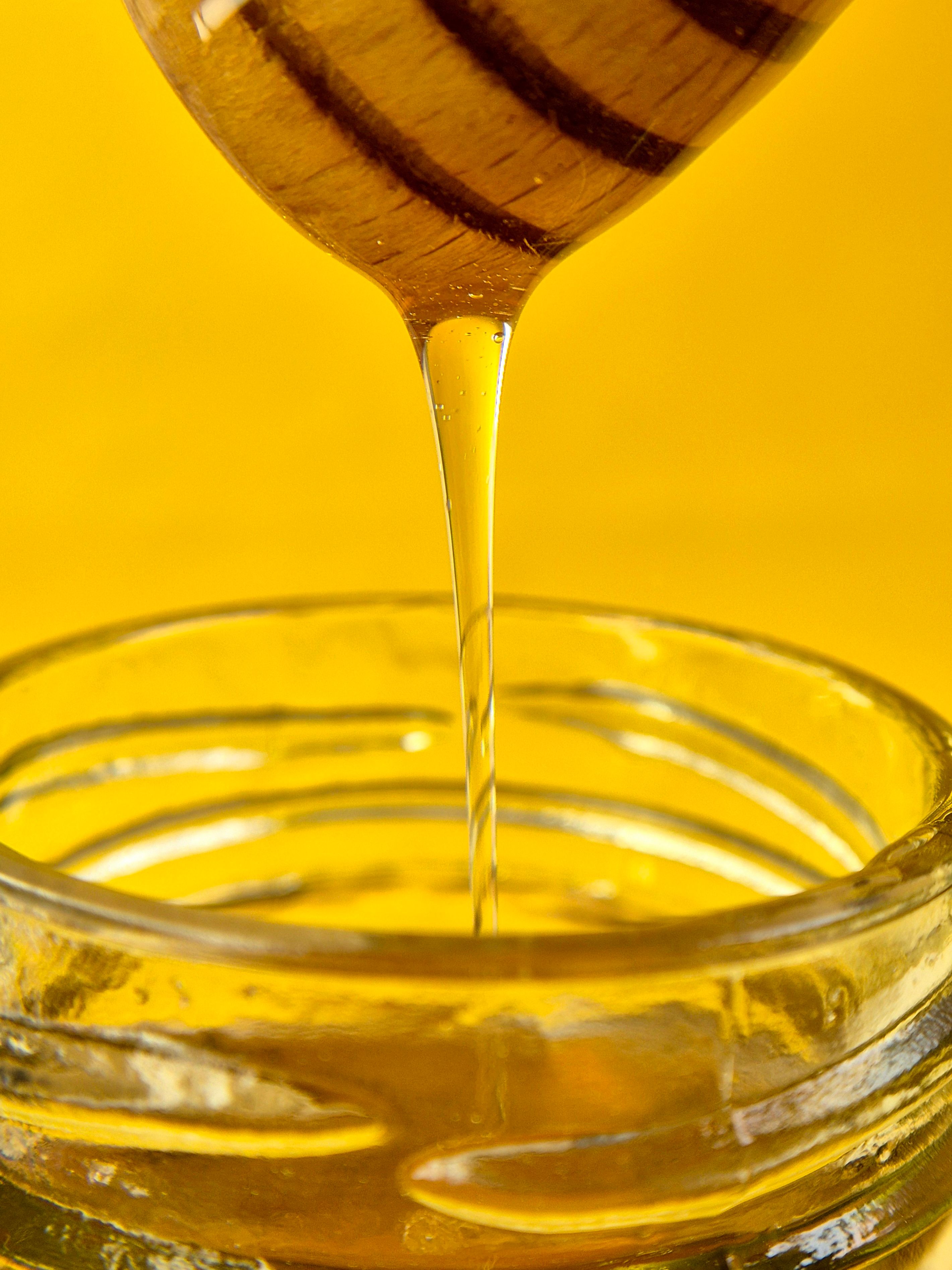 Close-up of golden honey flowing from dipper into a glass jar against a yellow background. - Evaluating Pricing and Value for Money