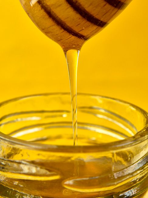 Close-up of golden honey flowing from dipper into a glass jar against a yellow background. - Evaluating Pricing and Value for Money