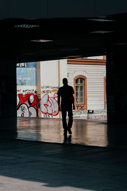 Free Silhouette of a man walking through a tunnel decorated with colorful graffiti in an urban setting. Stock Photo
