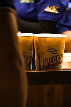 Vertical shot of popcorn buckets illuminated at a movie theater concession stand, capturing a cinematic snack moment.
