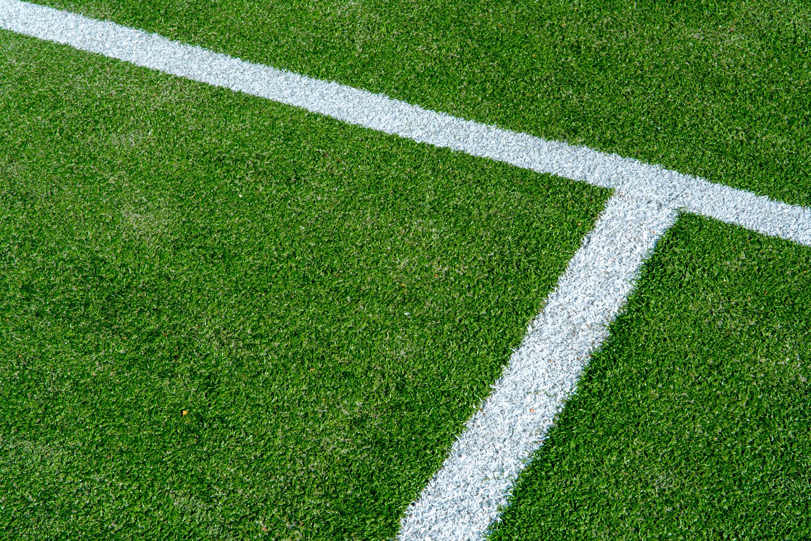 Close-up of intersecting white sports field lines on green turf