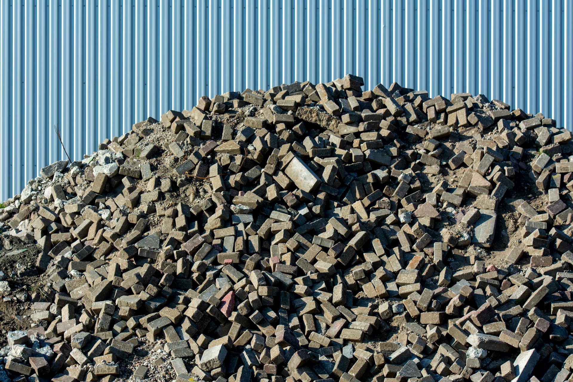 A large pile of rubble consisting of bricks and debris against a corrugated metal fence.