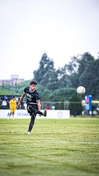 Teen soccer player kicking a ball during a match on a grassy sports field.