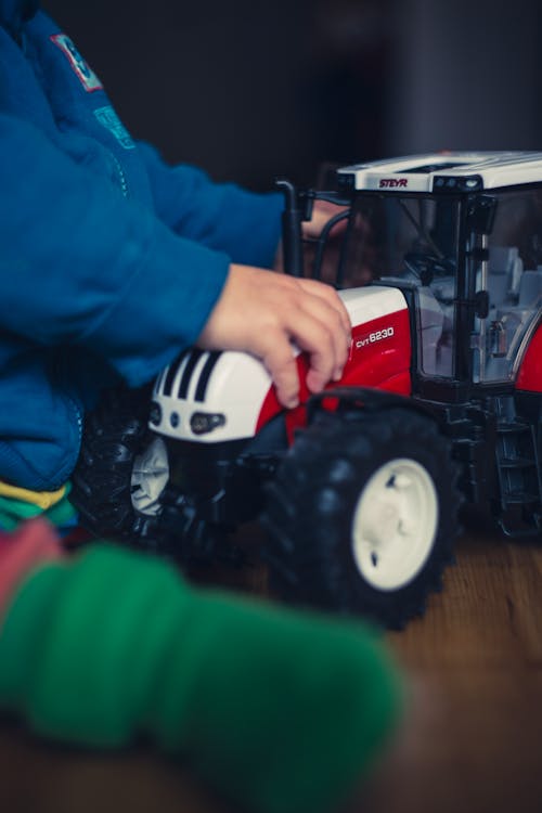 Free Person in Blue Jacket Holding Red and White Tractor Toy Stock Photo