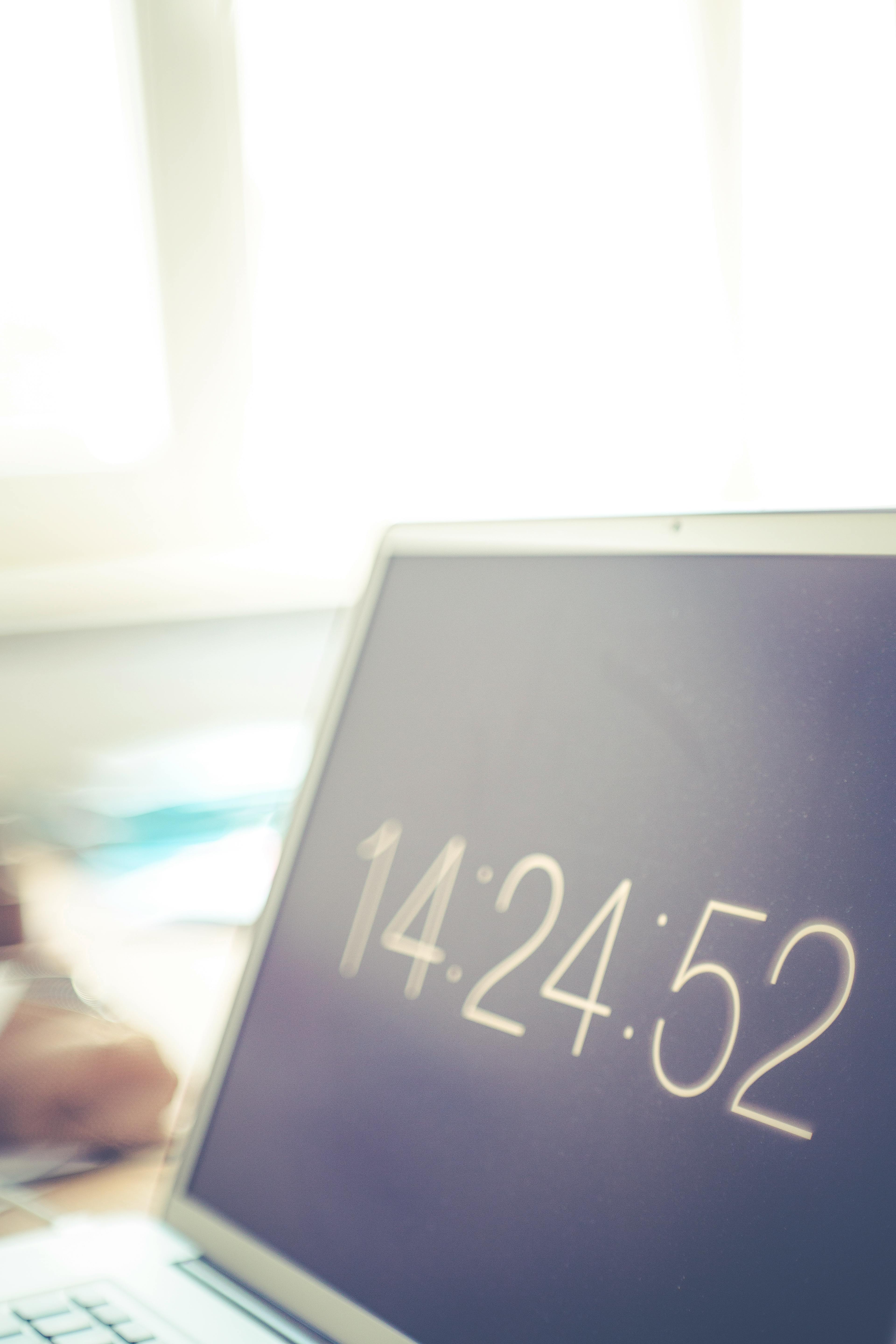 笔记本电脑屏幕上显示着数字时钟，背景是明亮的模糊办公室