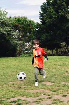 A cheerful child playing soccer in a lush green park, enjoying a sunny outdoor day.