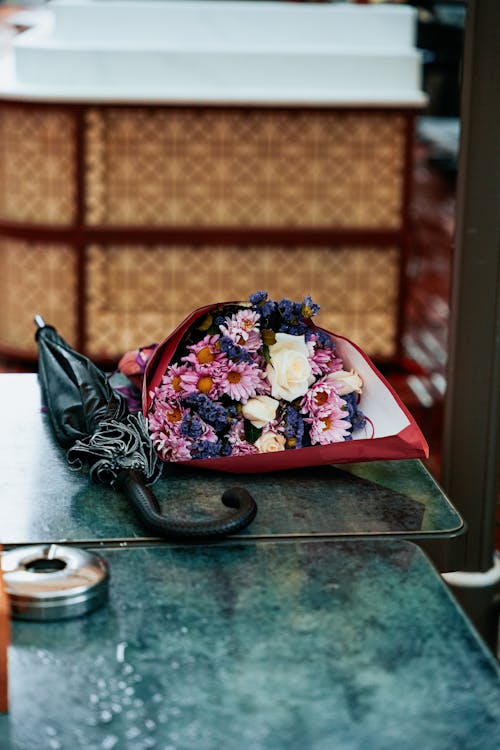 A bouquet of flowers sits on a table next to an umbrella