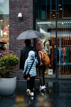 A family walks under an umbrella past a city store on a rainy day.