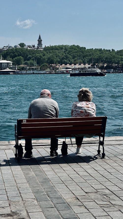 An elderly couple sitting on a bench overlooking the water