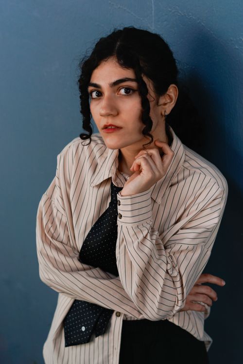 Free Portrait of an elegant woman with curly hair in a striped shirt and tie, posing in a studio setting. Stock Photo