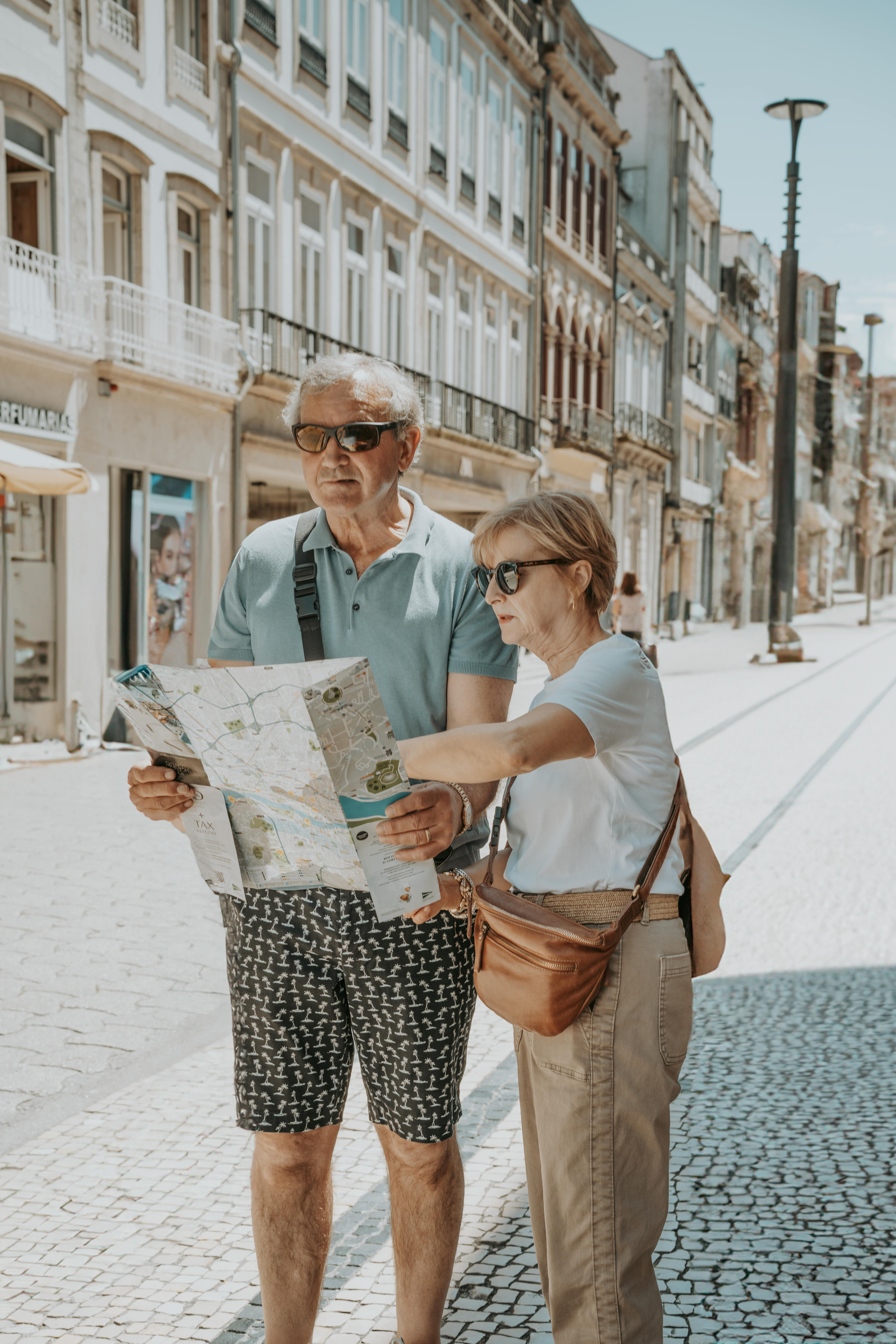 Senior couple in summer attire navigates with a map on a sunny Porto street.