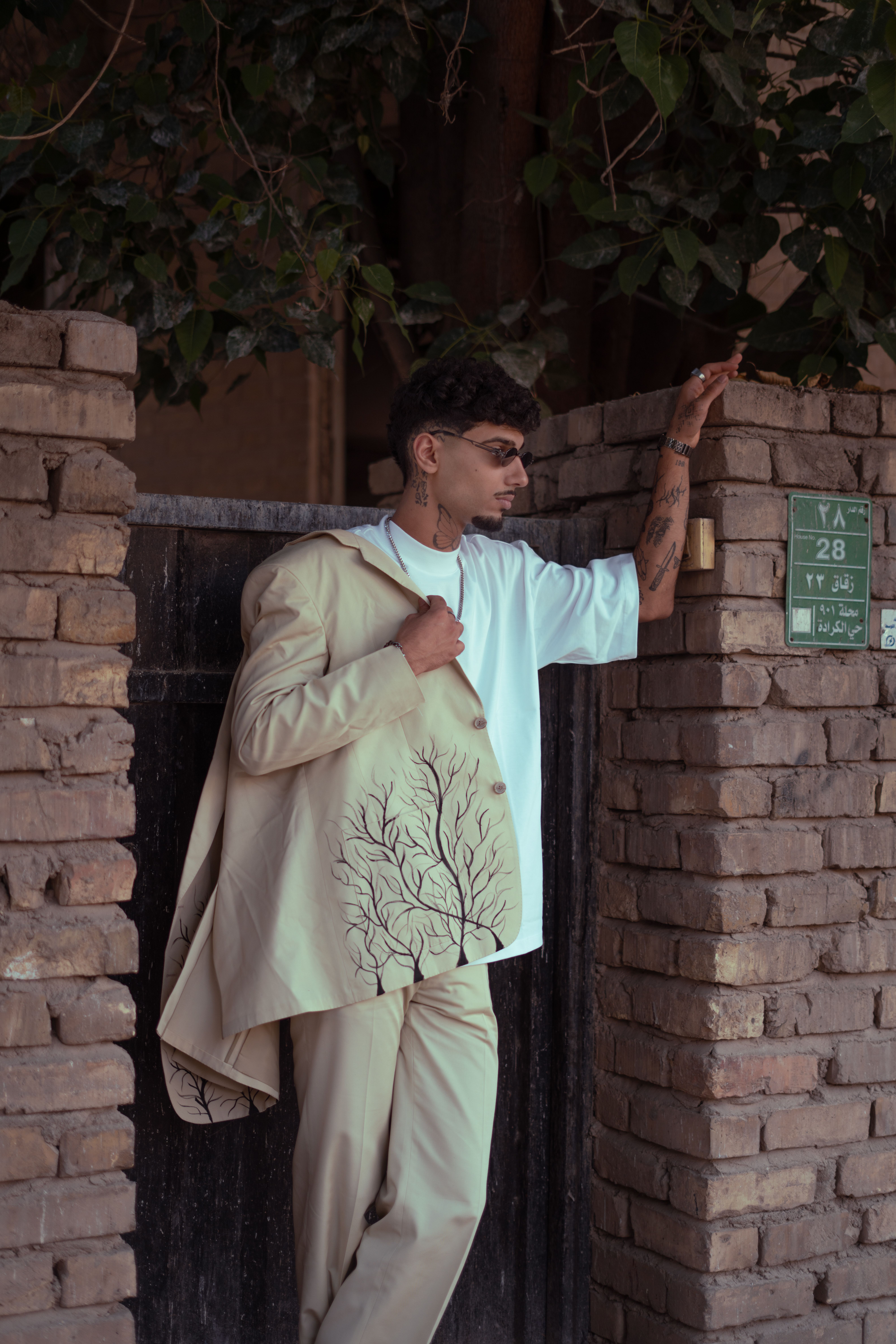 A young man in sunglasses poses fashionably against a stone wall in Baghdad, showcasing modern style.