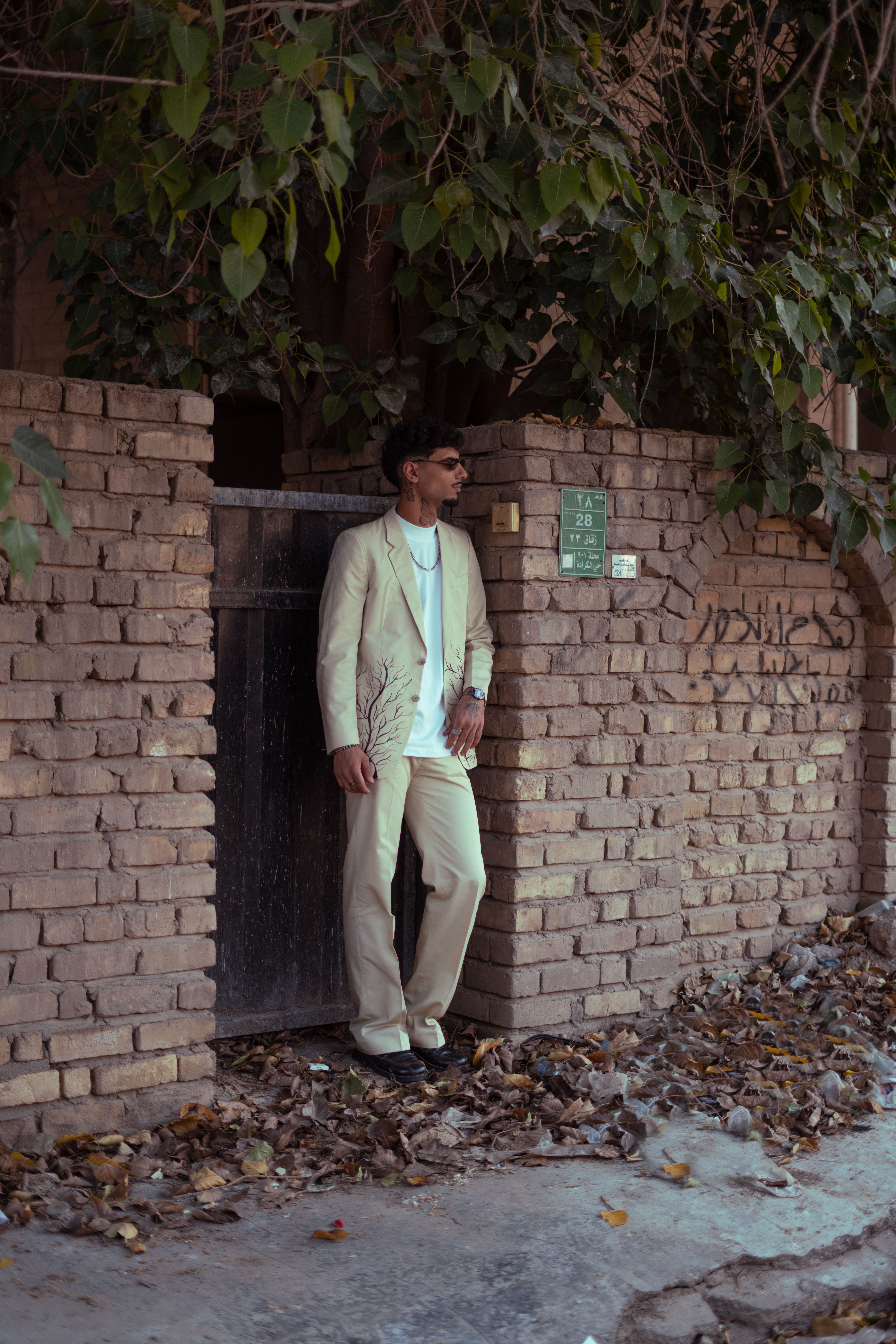 Young man in sunglasses and suit posing against a brick wall in Baghdad.