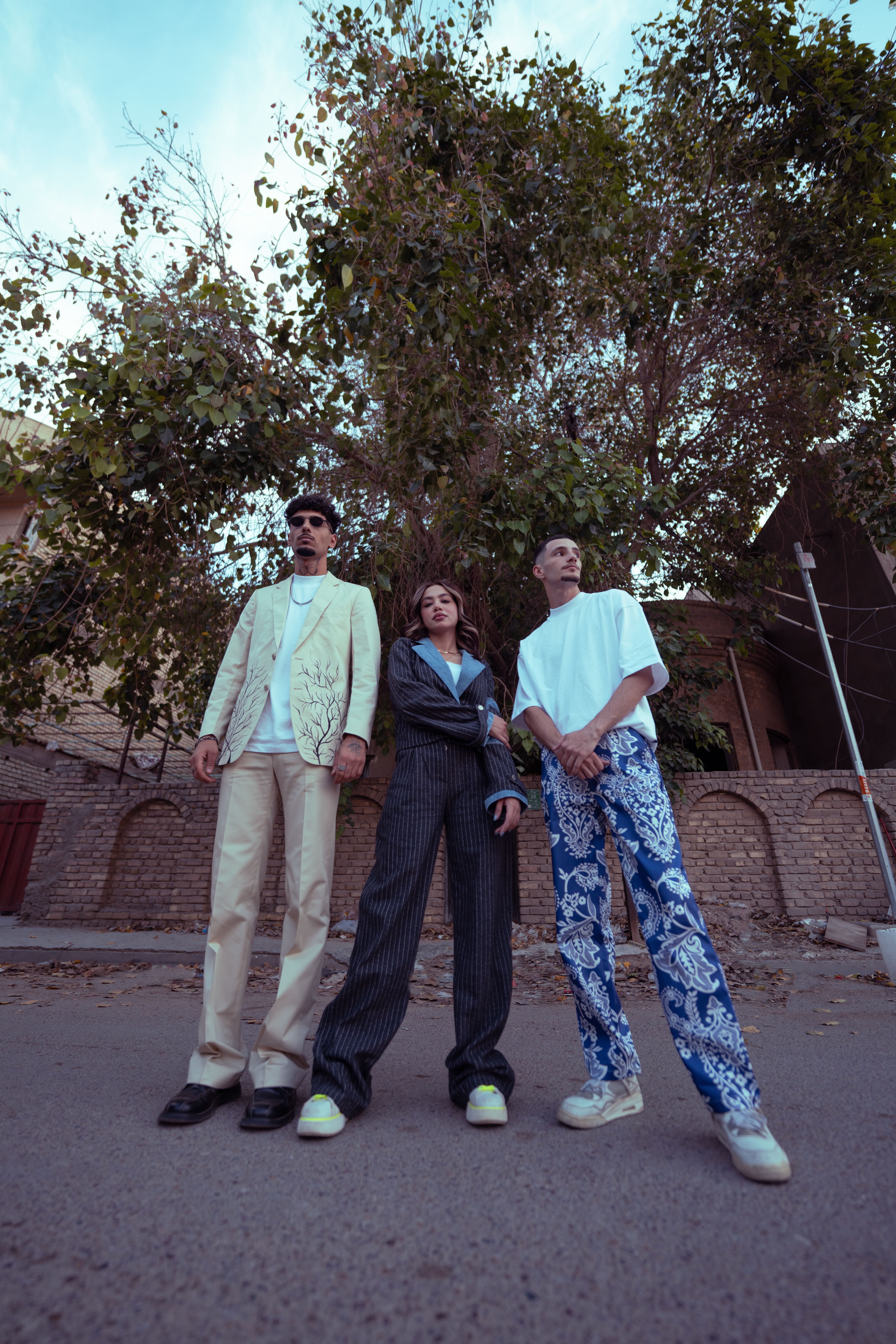Three fashionable adults pose confidently on an urban street in Baghdad, reflecting modern style.