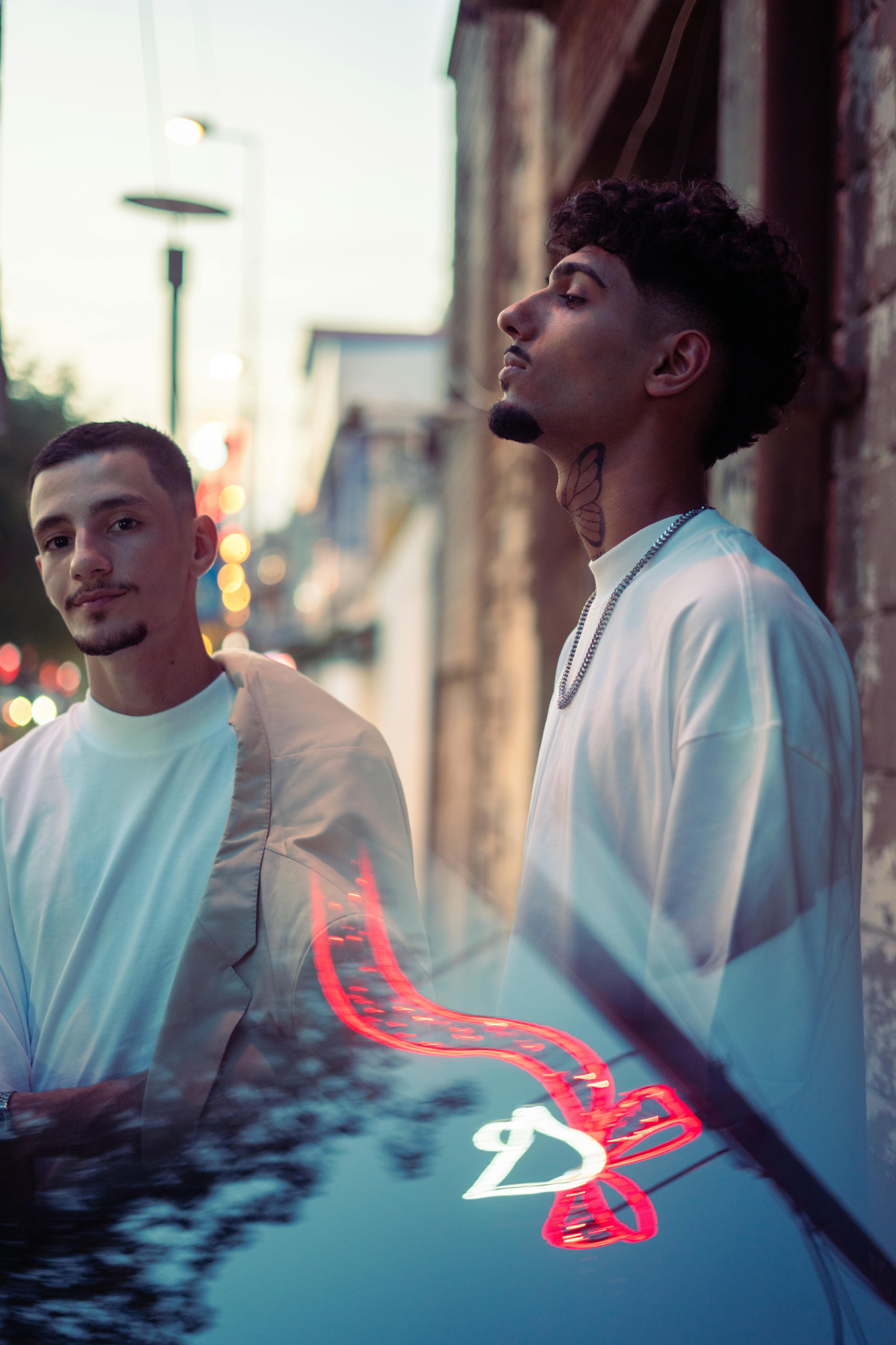 Two men posing outdoors with urban reflections in Baghdad, Iraq at dusk.