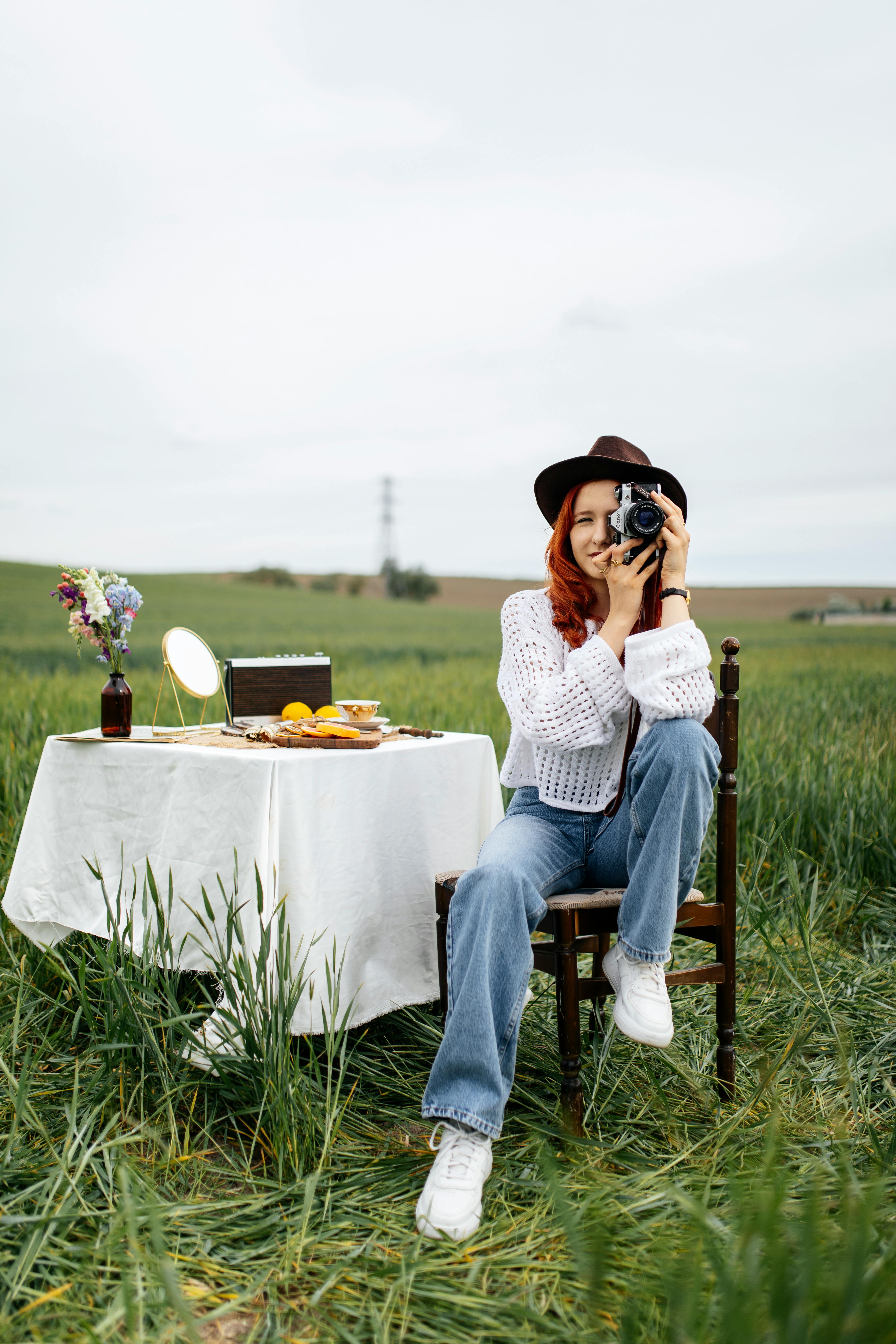 A woman sits in a field with a camera, capturing the serene outdoor setting.