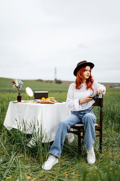 A woman sitting on a chair in a field with a table and a bottle of wine