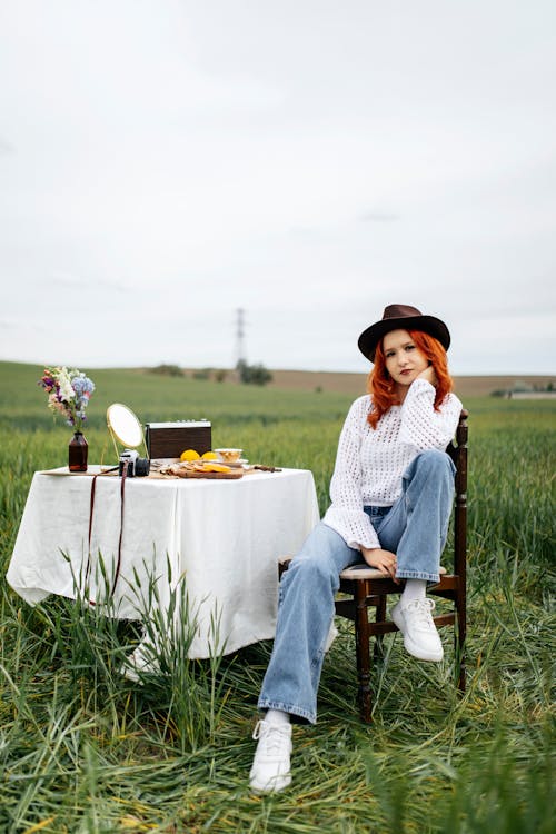A woman sitting on a chair in a field with a table and a white tablecloth