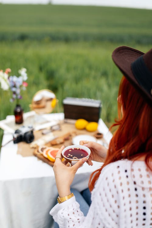 A woman with red hair and a hat is sitting on a picnic table