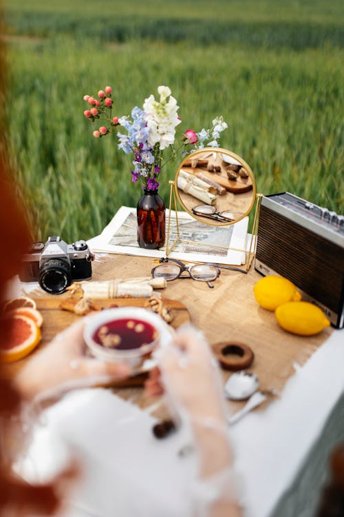 A woman is sitting on a table in a field with a camera and a cup of tea