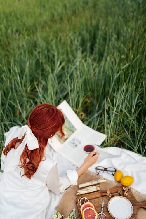 A woman with red hair sitting in a field with a book