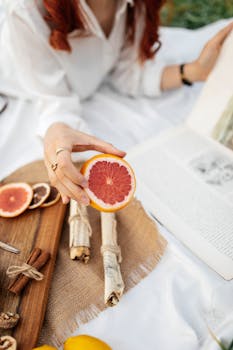 Redhead woman at a picnic holding a grapefruit slice, reading outdoors.