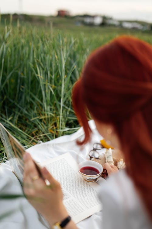 A woman with red hair reading a book in a field