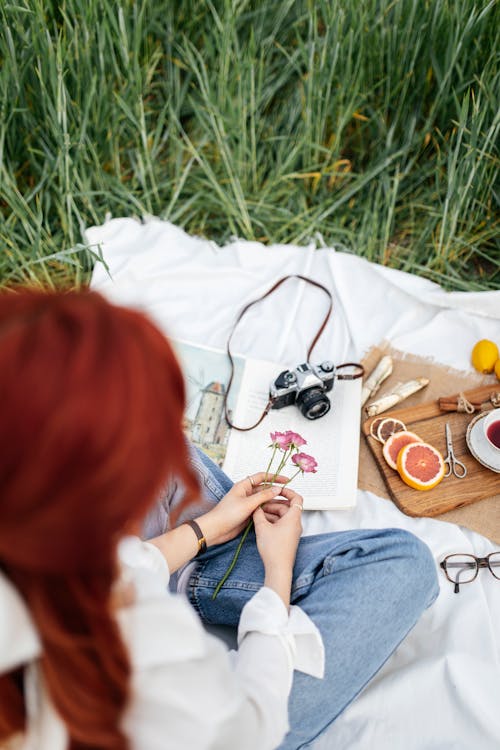 A woman sitting on the grass with a camera and a book