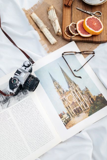 Vintage camera with open book, eyeglasses, and grapefruit slices on white cloth.