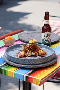 A gourmet dish served with Allende beer on a colorful tablecloth outdoors.