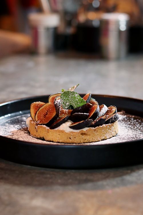 Free Close-up of a delicious fig tart on a black plate with a cozy indoor ambiance. Perfect for food photography. Stock Photo