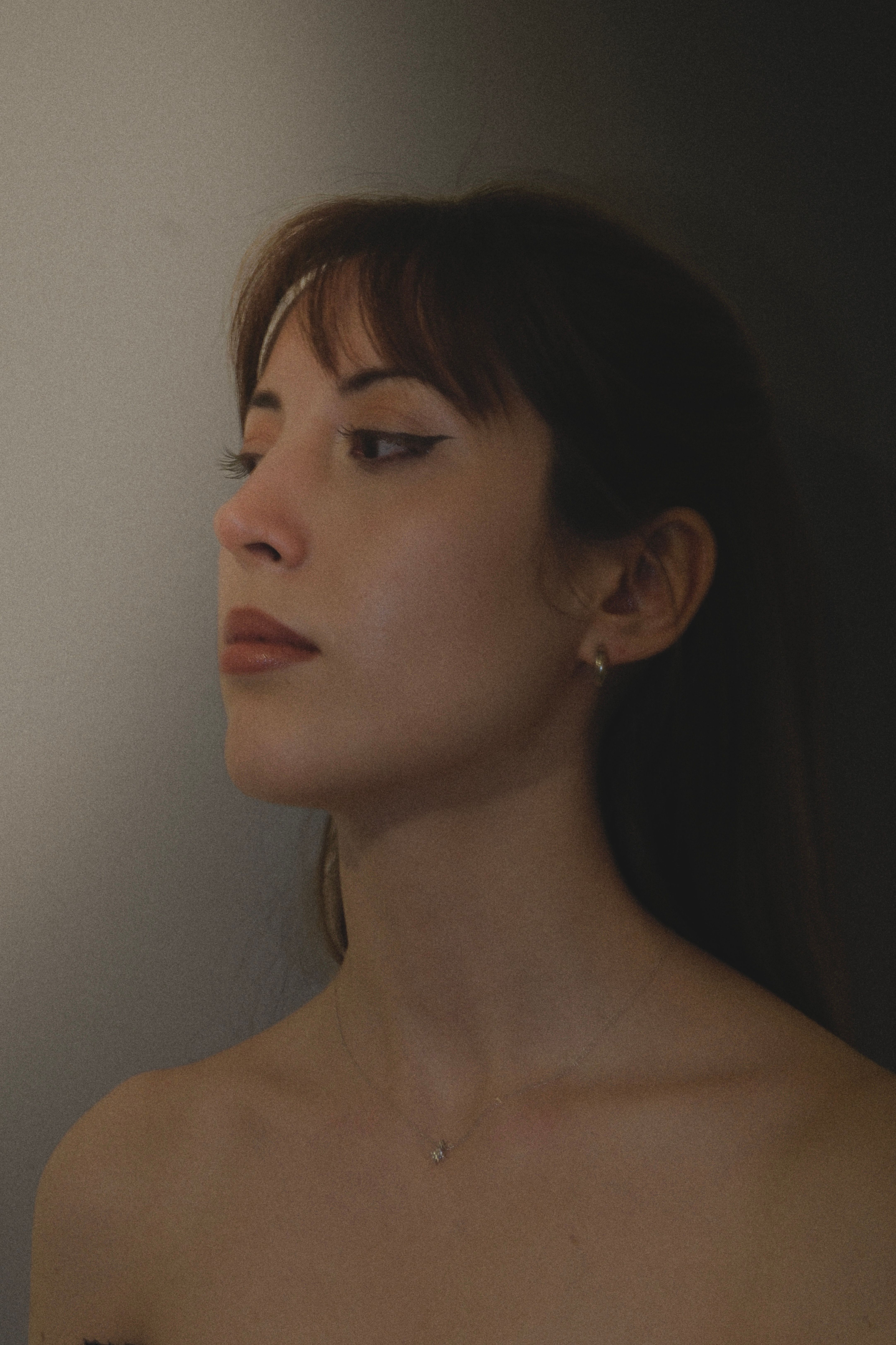Side profile of a young woman with bangs posing against a dark backdrop in Ankara, Türkiye.