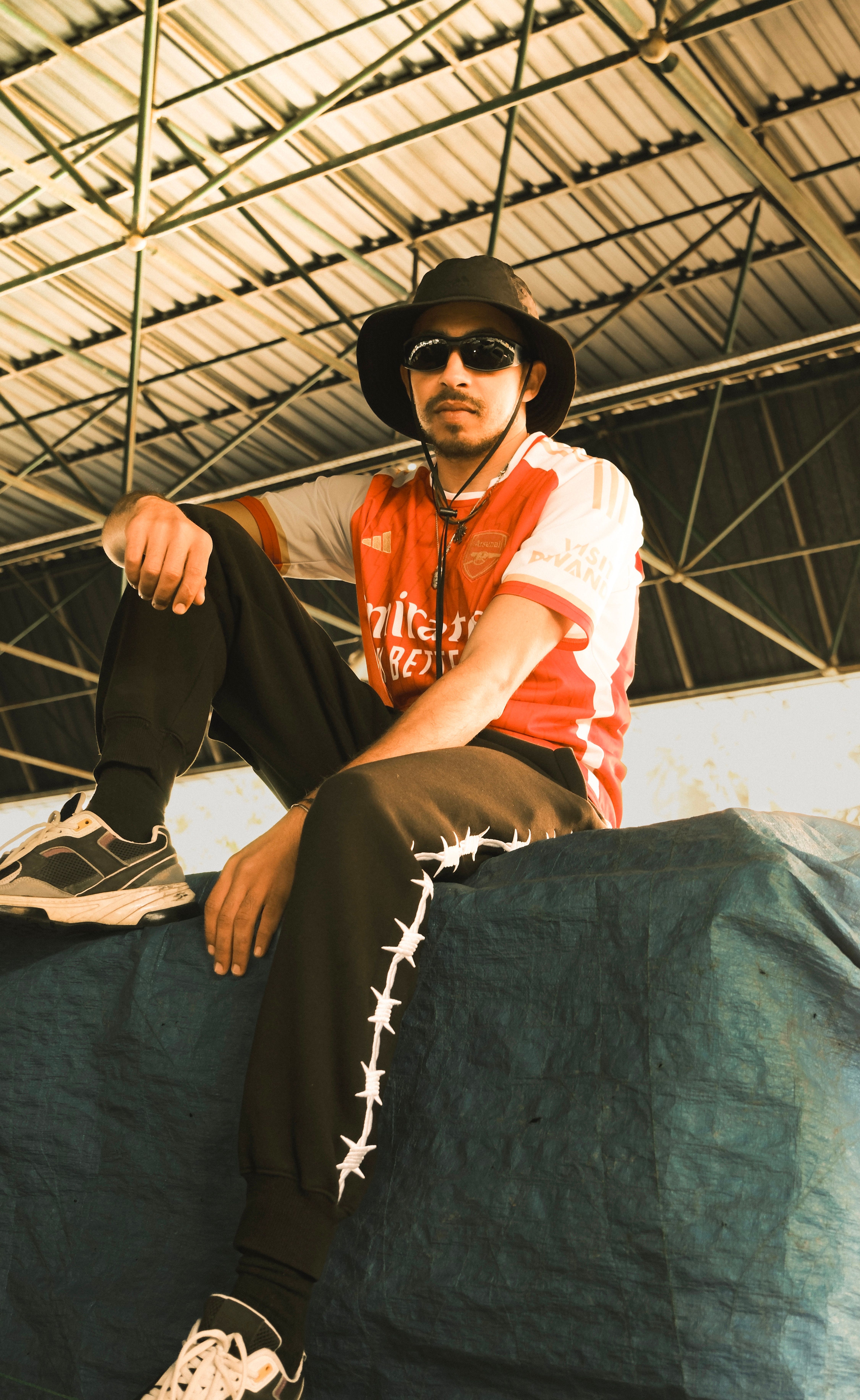 Young man in sunglasses seated casually in Ankara, displaying urban fashion style with sportswear.