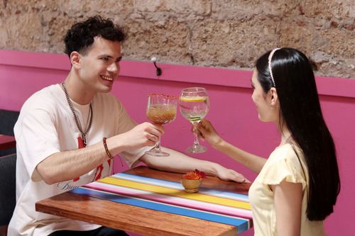 Free A joyful couple raising glasses in a colorful cafe, celebrating a cheerful moment. Stock Photo